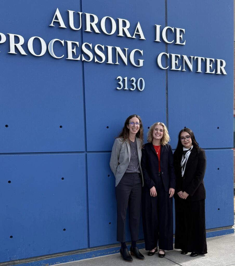 Three people standing in front of the Aurora ICE Detention Center